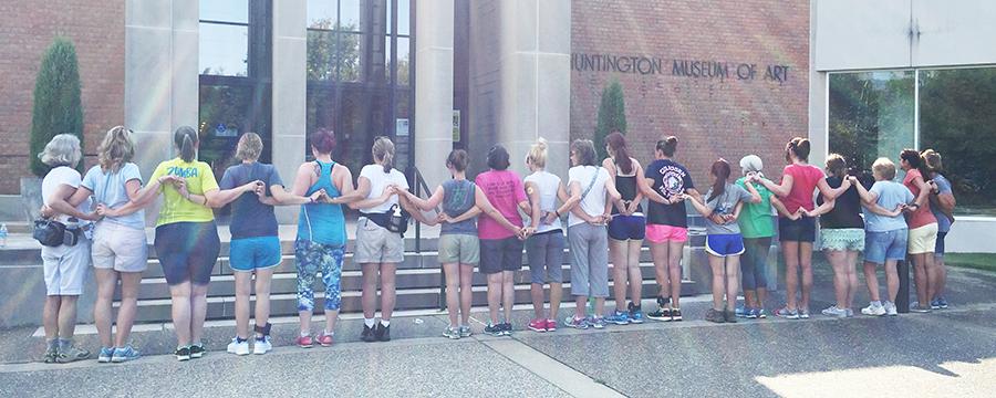 Participants of the WEAR program and volunteers link arms, forming hearts with their hands, outside the Huntington Museum of Art on Tuesday before their group hike. 