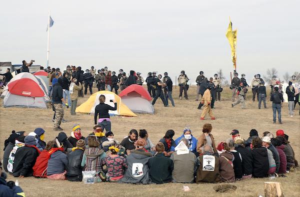 FILE - In this Oct. 27, 2016 file photo, Dakota Access Pipeline protesters sit in a prayer circle at the Front Line Camp as a line of law enforcement officers make their way across the camp to remove the protesters and relocate to the overflow camp a few miles to the south on Highway 1806 in Morton County, N.D. Members of more than 200 tribes from across North America have come to the Standing Rock Sioux Tribes encampment at the confluence of the Missouri and Cannonball rivers since August, the tribe says. Estimates at the protest site have varied from a few hundred to several thousand depending on the day _ enough for tribal officials to call it one of the largest gatherings of Native Americans in a century or more. (Mike McCleary/The Bismarck Tribune via AP, File)