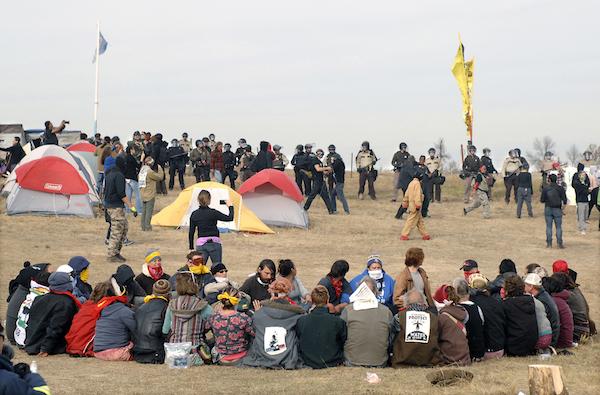 FILE - In this Oct. 27, 2016 file photo, Dakota Access Pipeline protesters sit in a prayer circle at the Front Line Camp as a line of law enforcement officers make their way across the camp to remove the protesters and relocate to the overflow camp a few miles to the south on Highway 1806 in Morton County, N.D. Members of more than 200 tribes from across North America have come to the Standing Rock Sioux Tribe's encampment at the confluence of the Missouri and Cannonball rivers since August, the tribe says. Estimates at the protest site have varied from a few hundred to several thousand depending on the day _ enough for tribal officials to call it one of the largest gatherings of Native Americans in a century or more. (Mike McCleary/The Bismarck Tribune via AP, File)