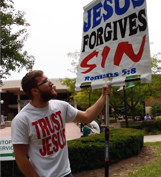 Zach Humphrey holds a sign while open-air preaching Monday outside the Memorial Student Center. Humphrey normally preaches alone, but brought a small team of preachers to join him Monday, attracting a crowd of Marshall students voicing their opposition to his positions.