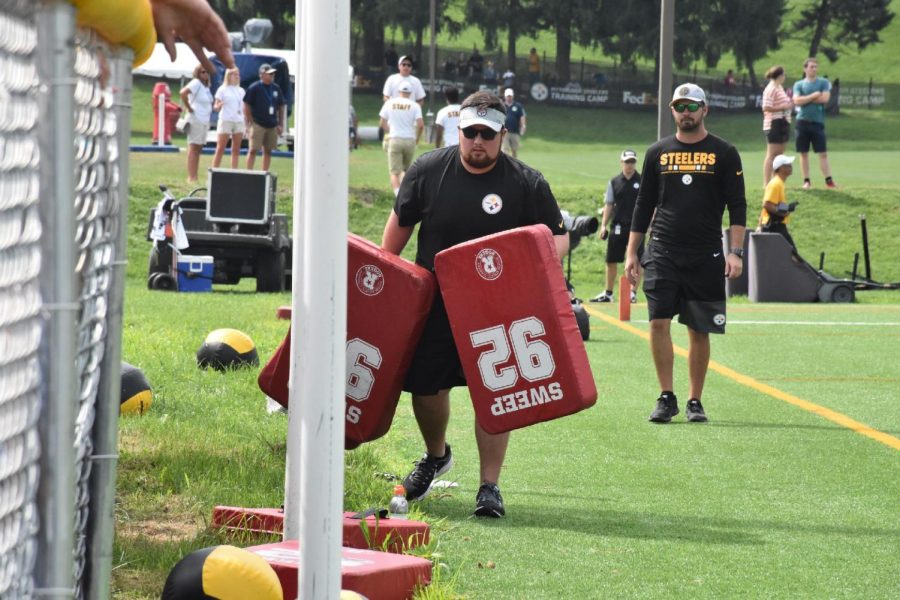 Kyle Powers (left) carries equipment at the Steelers’ training camp as an assistant coach looks on. Powers has similar duties for Marshall’s athletic program during the school year.