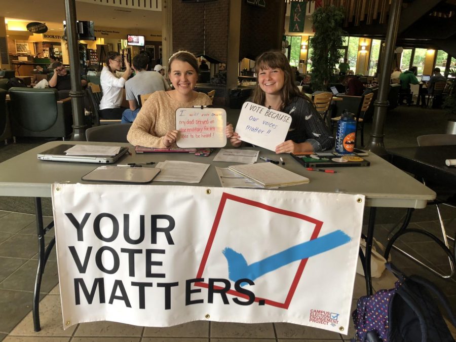 Madison Parker, left, Paige Looney, right, hold up signs to show why they vote in the lobby of the Memorial Student Center.