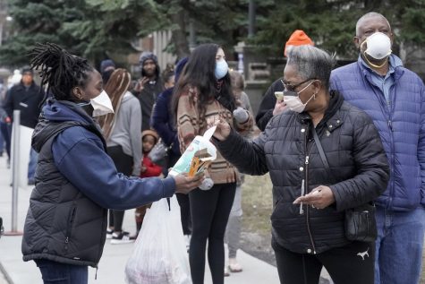 A worker hands out disinfectant wipes and pens as voters line up outside Riverside High School for Wisconsin’s primary election Tuesday, April 7, 2020, in Milwaukee.